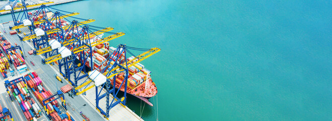 Aerial view of container port with colorful cranes loading cargo ship beside turquoise sea during...