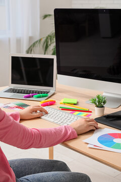 Female graphic designer working with laptop, computer, stationery and color palettes at table in office, closeup
