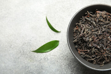 Naklejka premium Bowl of dry black tea leaves on grey grunge background