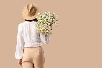 Obraz premium Young woman in wicker hat with bouquet of chamomile flowers on beige background, back view