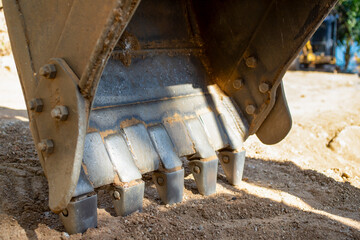 Close-up of excavator bucket with metal teeth touching soil. Detailed view of construction equipment during earthworks in tropical setting. © Max