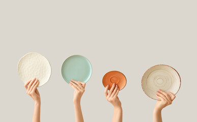 Hands holding empty plates on light background