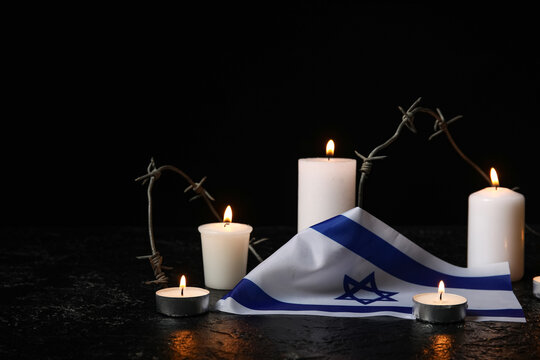 Burning candles, barbed wire and flag of Israel on dark background. Holocaust Remembrance Day
