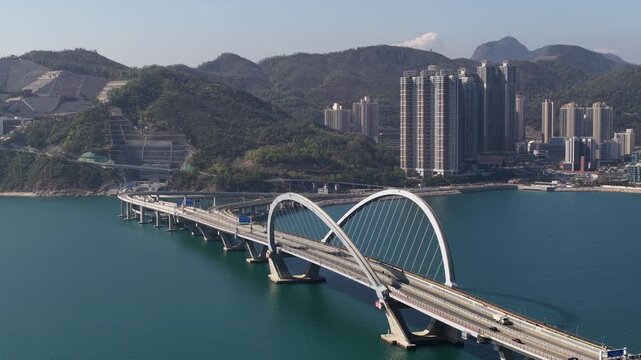 Stunning aerial perspective capturing the magnificent architecture of the tseung kwan o cross bay bridge, with traffic flowing smoothly against the backdrop of a modern city and mountains