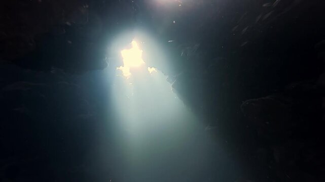 Mystical Sunbeams Piercing Through Dark Underwater Cave Entrance During Summer At Crystal Clear Tropical Lagoon Featuring Ethereal Tyndall Effect With Deep Blue Shadows And Low Angle Perspective View