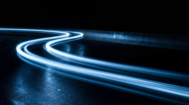 Long exposure photograph of bright blue light trails on a dark, wet, winding road at night.