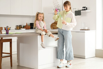 Nanny with little girl blowing soap bubbles in kitchen