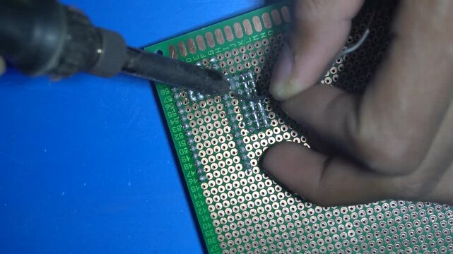 Close up of technician soldering electronic components on green prototype circuit board