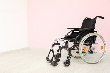 Naklejka premium Modern empty wheelchair near pink wall