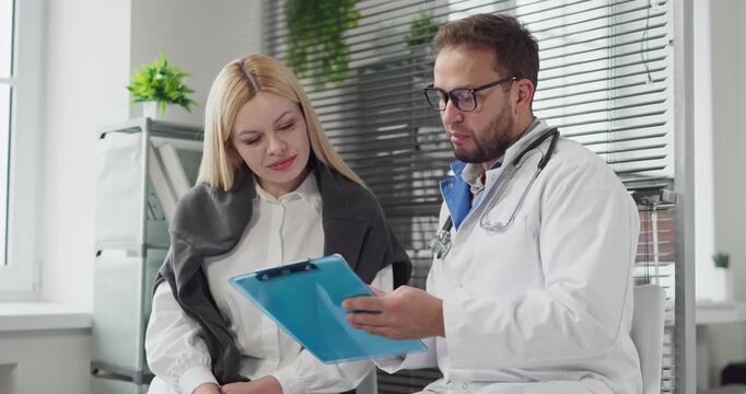 Doctor and patient consultation in medical office. The clinician offers advice during a clinic appointment, reviewing a clipboard with empathy. Patient centered healthcare consultation concept.
