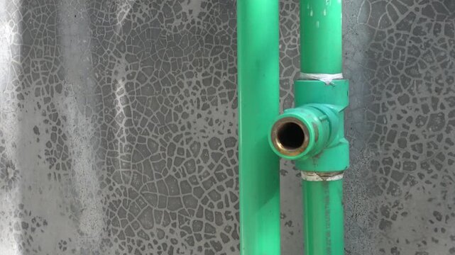 Plumbing system with green pipes and brass fitting on a textured wall