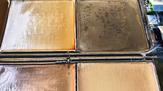 4K aerial drone footage over salt evaporation ponds with vibrant geometric patterns. Colorful abstract textures and structured coastal landscape in Thailand.
