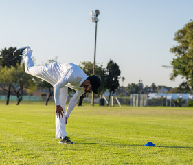 Obraz premium Mid-adult man balancing on sports field wearing white kit, black cap, gray shoes, blue cone nearby