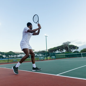 African American man in white holding racket preparing swing near net with tennis ball, copy space