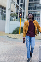 Mid adult African American man walking across office plaza pulling suitcase with phone, copy space © wavebreak3