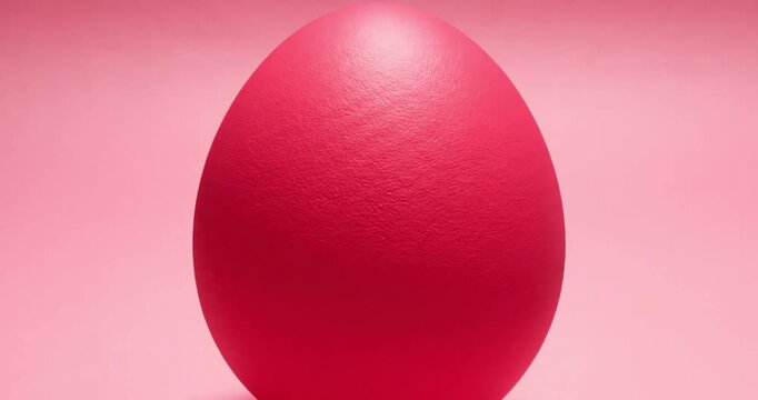 A single, vibrant magenta-pink egg gracefully rolls into view on a soft, monochromatic pink background, pausing momentarily before slowly exiting the frame. The minimalist composition, combined with t