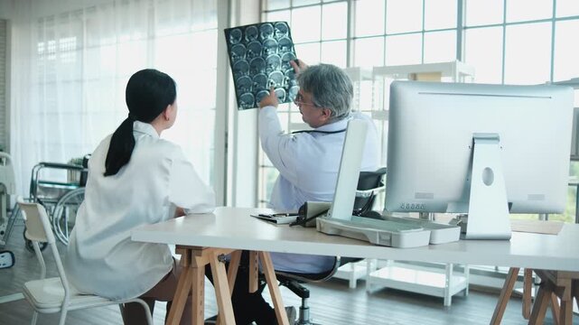 Professional radiology doctor explains X-ray film, brain scan results to senior Asian female patient, medical consultation, and health checkup in hospital, diagnosis advice, and sickness treatment.