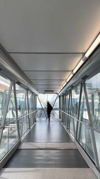 Latin american female tourist wearing a straw hat and backpack walking along a modern glass and steel terminal jet bridge towards a luxury cruise ship in Miami, Florida during a vacation trip