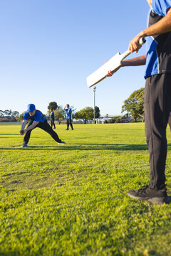 White cricket bat leaning on cricket field under blue sky with floodlight pole and trees