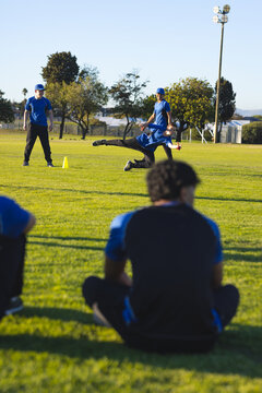 Diving baseball player reaching out on practice field, with teammate supporting next to yellow cone