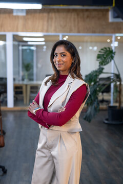 Indian woman posing in office wearing burgundy top, showcasing smartwatch amid glass partitions