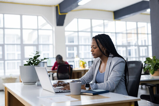 Diverse coworkers in business casual attire working on laptop in office with coffee mug, copy space