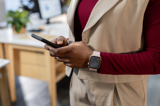 Indian woman holding smartphone and checking messages at office desk with smartwatch and plant