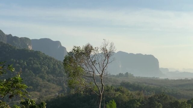 Soft sunrise light over forest hills and distant limestone mountains at Din Daeng Doi in Krabi Thailand with gentle haze, layered landscape, and calm natural scenery