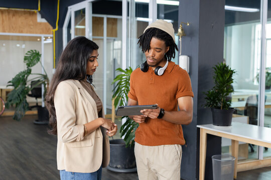Diverse coworkers discussing project on digital tablet in open plan office with glass partitions