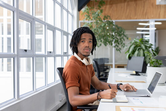 African American man sitting at desk in open-plan office reviewing charts next to silver laptop