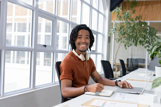 African American man reviewing printed charts at office desk wearing polo shirt and headphones