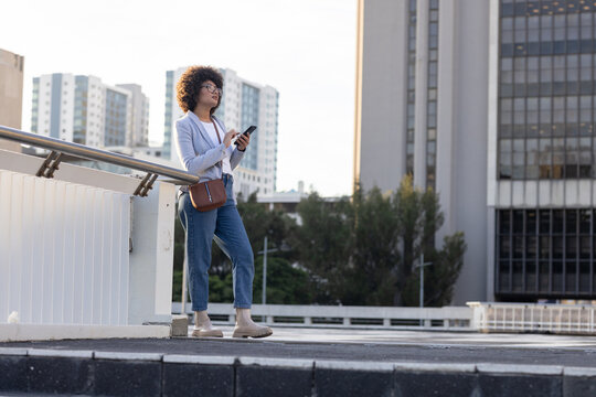 Woman holding smartphone and leather bag on overpass next to metal railing