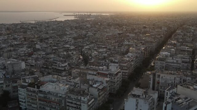 Aerial establishing shot of thessaloniki city in greece with the sun setting over the aegean sea