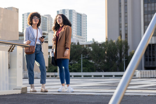 Diverse female coworkers with smartphone leaning on railing on rooftop parking deck, copy space