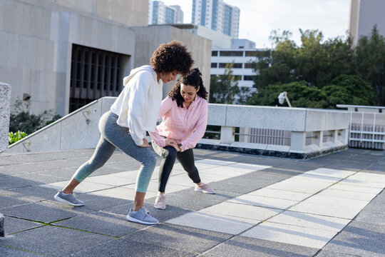 African american friends in sportswear lunging sideways on rooftop terrace, concrete railing