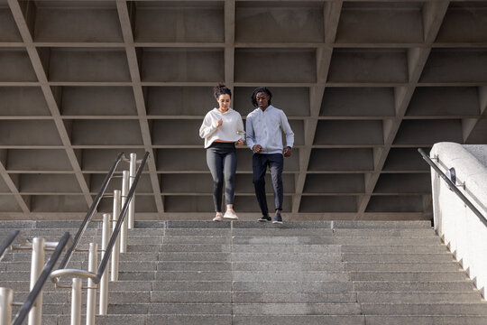 African american friends descending concrete stairs with metal handrails at plaza, workout