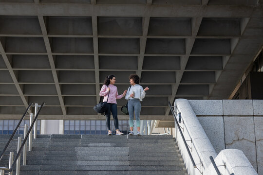 African american female friends standing on steps at entrance holding gym bags, water bottle