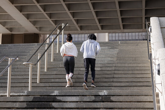 Diverse workout partners running up concrete stairs at civic entrance in hoodies
