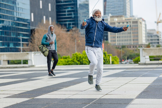 African american friends skipping with blue-handled rope and carrying olive duffel in city square