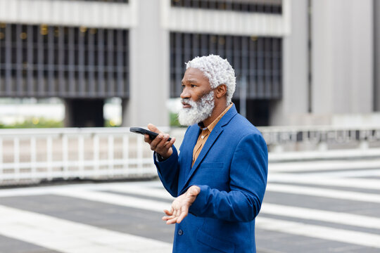 Senior african american man in blazer speaking into smartphone, gesturing at crossing