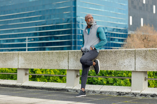 African american man sitting on barrier by railing at rooftop gazing, checking smartwatch