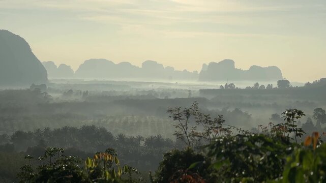 Misty valley at sunrise with distant limestone silhouettes and layered forest at Din Daeng Doi in Krabi Thailand showing soft haze, warm light, and peaceful landscape