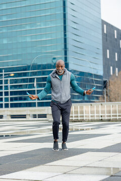 African american man jumping rope on plaza by glass office in sportswear with puddles