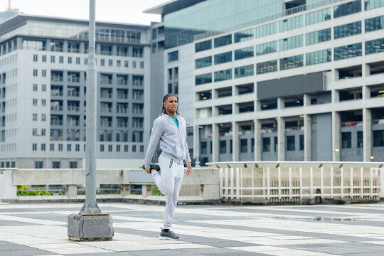 Adult man stretching leg on checkerboard rooftop tiles near lamppost concrete base