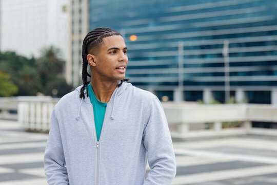 Man standing on rooftop plaza wearing gray zip-up hoodie and teal t-shirt