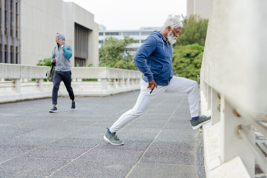 African american men stretching and walking on roof ledge carrying gym bag using phone