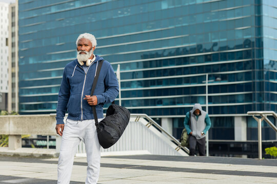 African american man walking across terrace carrying black duffel bag, white headphones