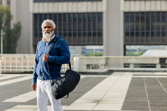African american man standing on office terrace wearing headphones and carrying duffel bag