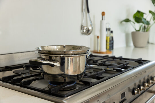Stainless steel saucepan with lid and nested pan sitting on front-left burner over blue flame