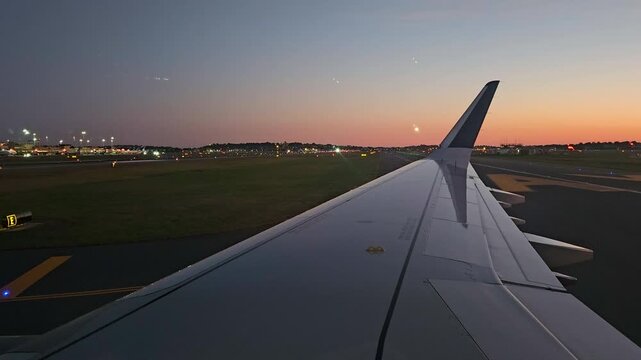 View across aircraft wing holding short on the taxiway as another aircraft takes off on the cross runway ahead in the early first light of morning. 